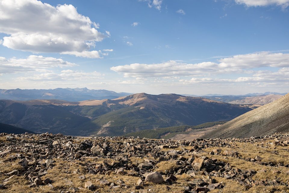Rocky alpine tundra in the foreground and a broad mountain valley below a cloud-streaked sky