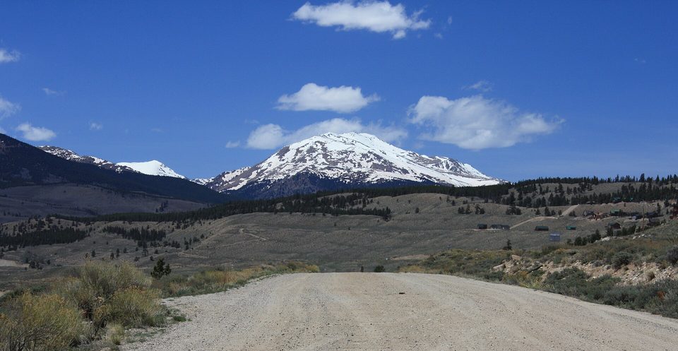 A gravel road heading toward snow-covered Mount Massive under a blue sky